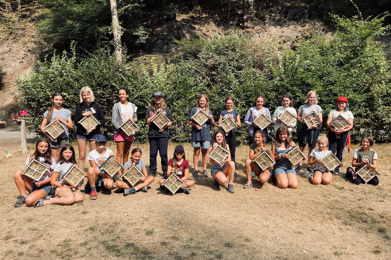 Glücklich präsentieren die jungen Teilnehmerinnen des Sommerferiencamps 2022 des Ada-Lovelace-Projekts im Pfadfinderlager Brexbachtal ihre selbstgebauten Insektenhotels. Bild: Universität Koblenz-Landau