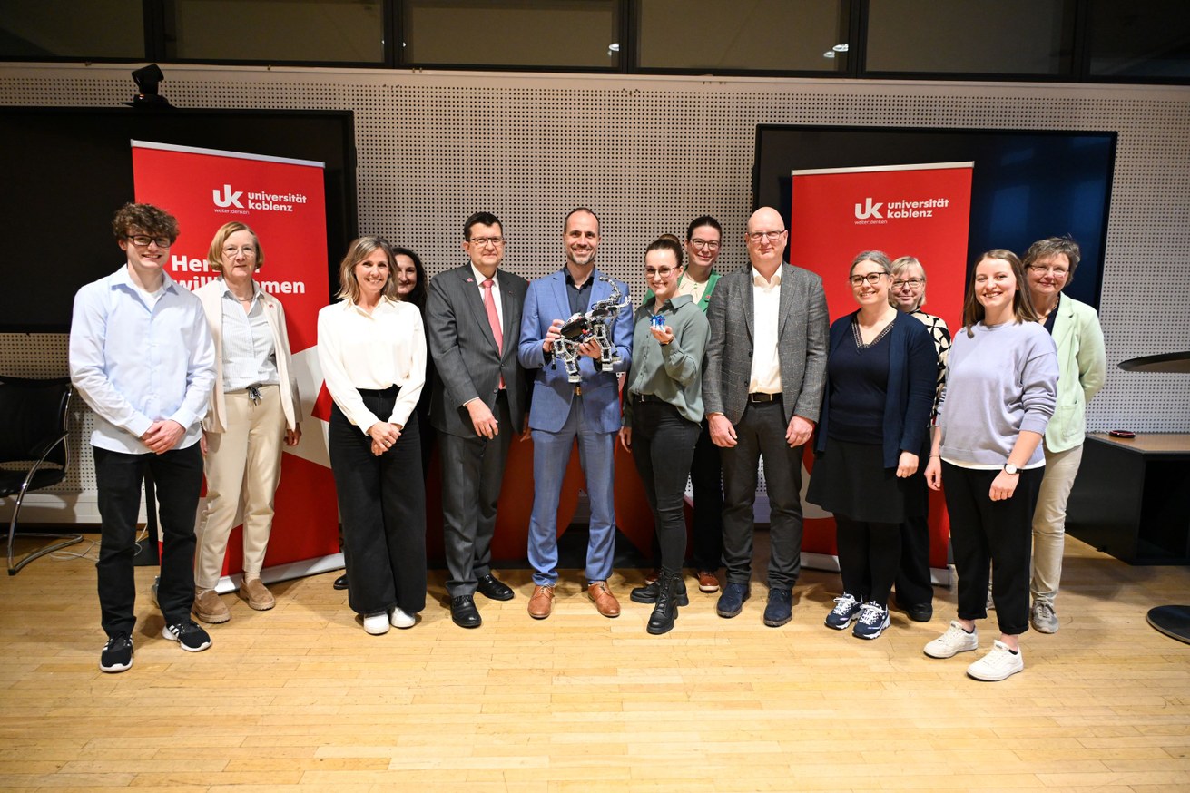 Präsident Prof. Dr. Stefan Wehner (5. v. l.) und Minister Clemens Hoch (6. v. l.) mit den Akteur*innen der Maßnahme Schnittstelle Schule-Hochschule an der Universität Koblenz. Der Minister hält den Roboter-Elefanten EV3-Roboter aus dem Roberta Lab der Universität. Bild: Universität Koblenz / Christoph Asche